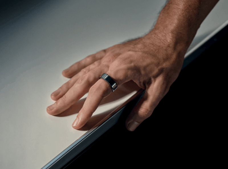 Mano apoyada sobre una superficie con un anillo wearable en el dedo, representando un dispositivo inteligente que monitoriza en silencio salud y recuperación